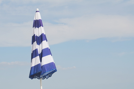 Blue and White Striped Closed Parasol against Summer Blue Skyの写真素材