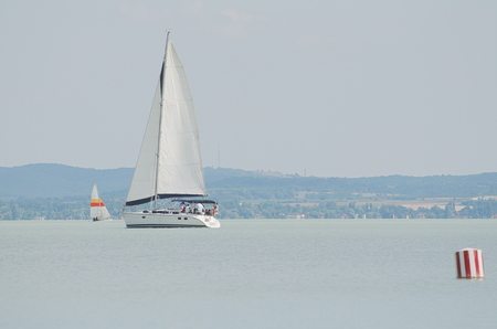 White Sailboat on Lake Balaton with Red and White Striped Buoyの写真素材