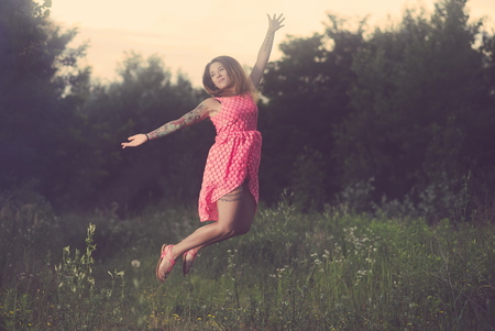 Young Tattooed Woman Jumping on a Forest Glade on a Summer Dayの写真素材