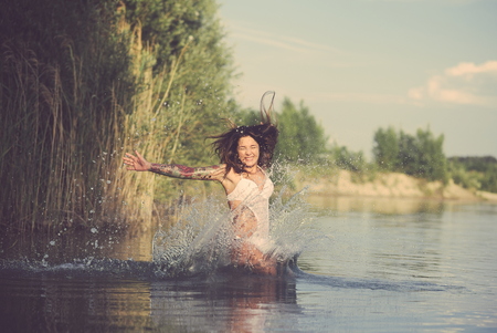 Young Tattooed Woman Jumping into Lake Water on a Summer Dayの写真素材