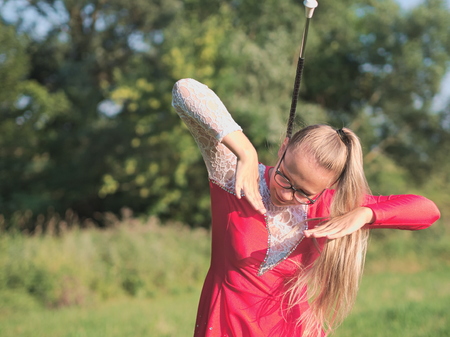 Bespectacled Blonde Teen Majorette Girl Twirling Baton Outdoors in Red Dressの写真素材