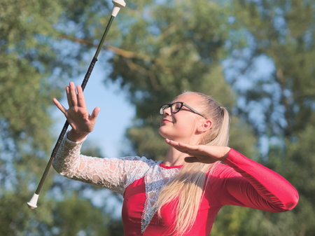 Bespectacled Blonde Teen Majorette Girl Twirling Baton Outdoors in Red Dressの写真素材