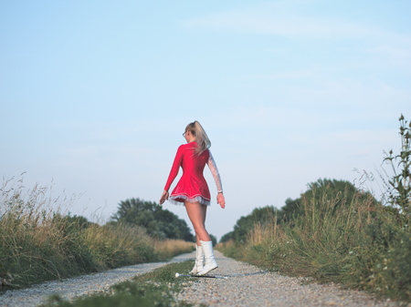 Bespectacled Blonde Teen Majorette Girl Twirling Baton Outdoors in Red Dressの写真素材