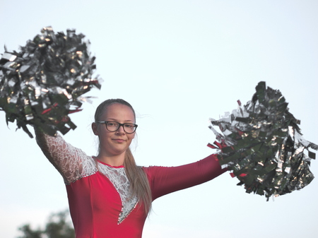 Bespectacled Blonde Teen Majorette Girl with Pom-poms Outdoors in Red Dressの写真素材