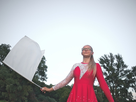 Bespectacled Blonde Teen Majorette Girl with White Flag Outdoors in Red Dressの写真素材