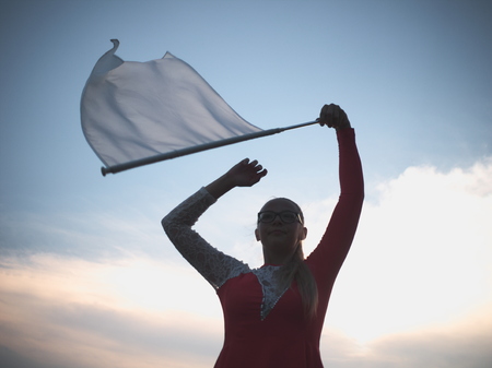 Bespectacled Blonde Teen Majorette Girl with White Flag Outdoors in Red Dressの写真素材