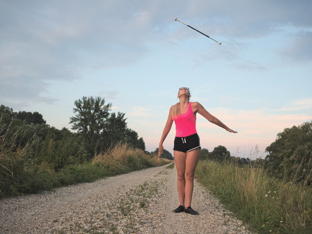 Bespectacled Blonde Teen Majorette Girl Twirling Baton Outdoors in Workout Clothingの写真素材