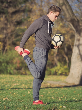 Soccer Player Stretching with Football in the Park on a Sunny Autumn Day