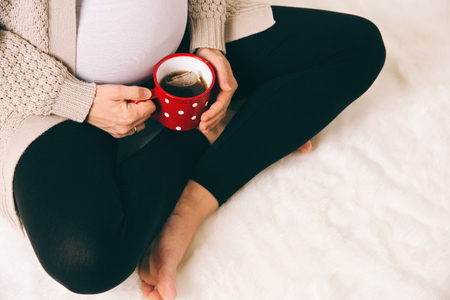 Pregnant Woman Sitting with Tea in Red Mugの写真素材