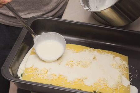 Pouring White Creamy Sauce with Ladle on Raw Spinach Lasagneの写真素材