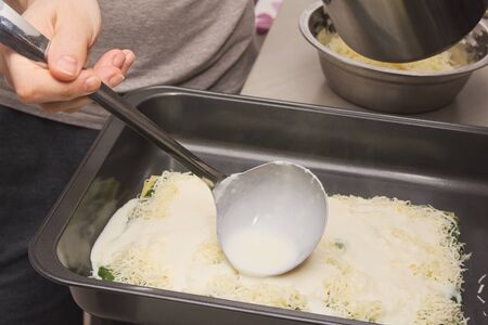 Pouring White Creamy Sauce with Ladle on Raw Spinach Lasagneの写真素材