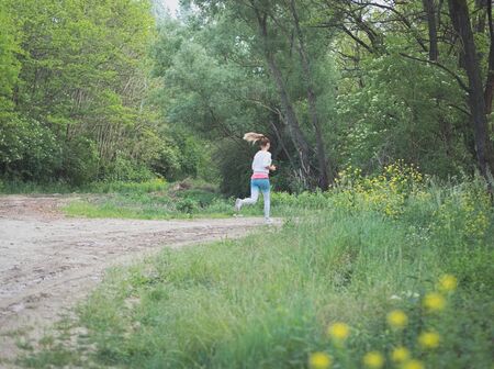 Young Blonde Caucasian Female Running in Forest on a Dirt Roadの写真素材