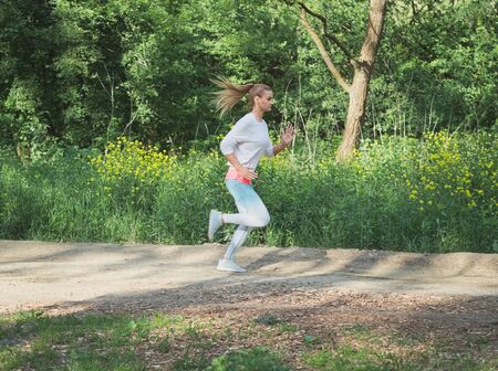 Young Blonde Caucasian Female Running in Forest on a Dirt Roadの写真素材