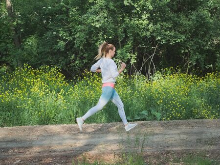 Young Blonde Caucasian Female Running in Forest on a Dirt Roadの写真素材