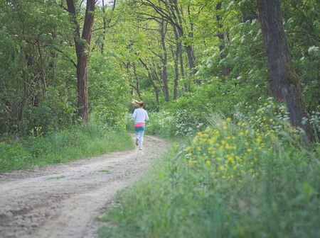 Young Blonde Caucasian Female Running in Forest on a Dirt Roadの写真素材