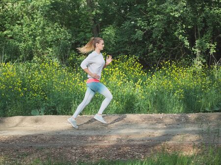 Young Blonde Caucasian Female Running in Forest on a Dirt Roadの写真素材
