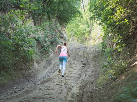 Young Blonde Caucasian Female Running in Forest on a Dirt Roadの写真素材