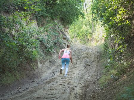 Young Blonde Caucasian Female Running in Forest on a Dirt Roadの写真素材