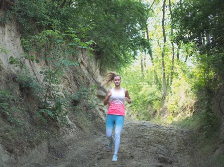 Young Blonde Caucasian Female Running in Forest on a Dirt Roadの写真素材