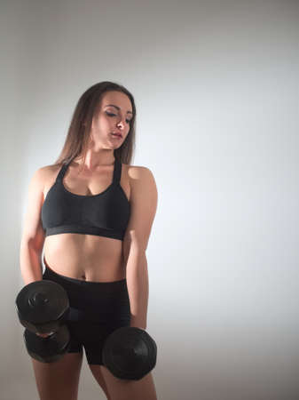Beautiful Young Brunette Woman Posing in Sportswear in the Studio with Dumbbellsの写真素材
