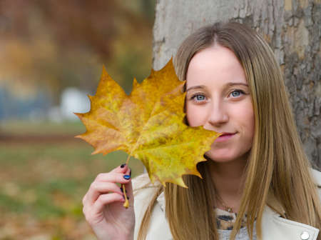 Portrait of a Young Beautiful Blonde Woman in Autumn Park with Maple Leafの写真素材