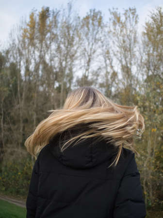 Back View of a Young Woman Tossing Her Long Blonde Hair in Autumn Parkの写真素材