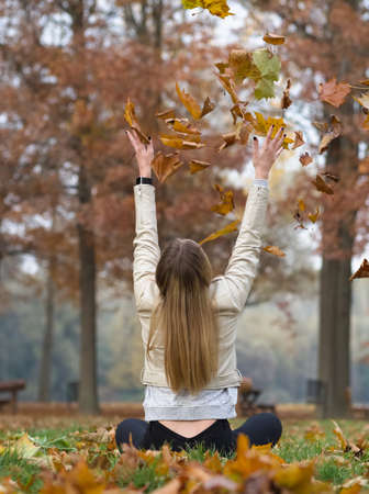Young Blonde Woman Sitting in Autumn Park Throwing Brown Maple Leaves