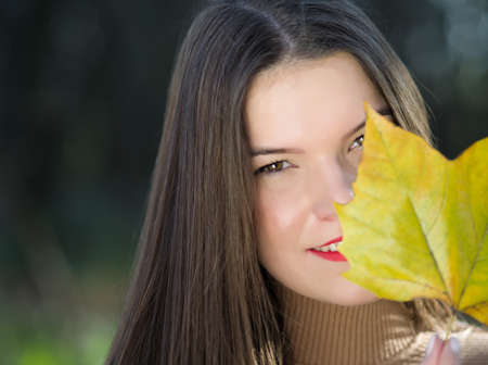 Portrait of a Young Beautiful Long Haired Brunette Woman with Maple Leafの写真素材