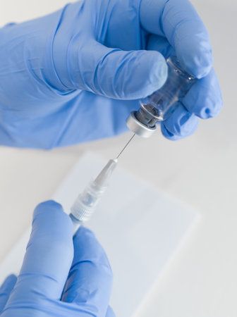 Hands in Blue Rubber Gloves Holding Medical Syringe and Vial Macro Closeup on White Backgroundの写真素材