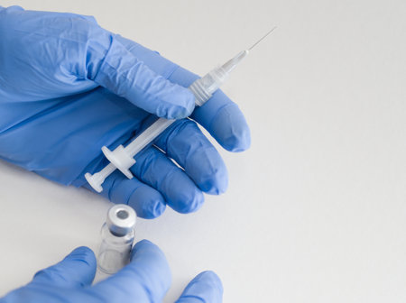 Hands in Blue Rubber Gloves Holding Medical Syringe and Vial Macro Closeup on White Backgroundの写真素材