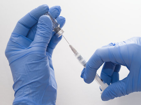 Hands in Blue Rubber Gloves Holding Medical Syringe and Vial Macro Closeup on White Backgroundの写真素材