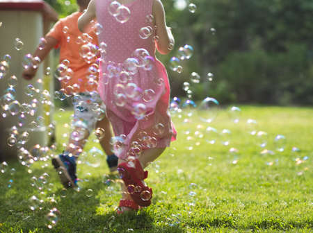 Children Running Through Soap Bubbles in the Yard on a Sunny Summer Day
