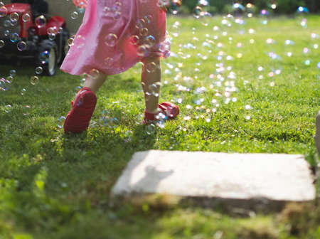 Little Girl in Pink Dress Running Through Soap Bubbles in the Yard