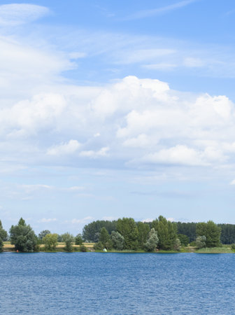 A tranquil scene of a blue sky above a lake, surrounded by lush trees and nature. A perfect escape from the hustle and bustle of everyday life.の写真素材