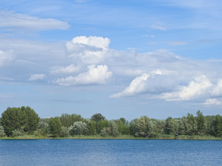 A beautiful, tranquil lake surrounded by trees and the blue sky with clouds above. Perfect for admiring nature's beauty in peace.の写真素材