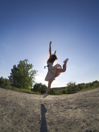 A fit girl dances outdoors in a floral dress under the sunny skyの写真素材