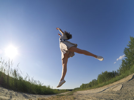 A fit girl dances outdoors in a floral dress under the sunny skyの写真素材