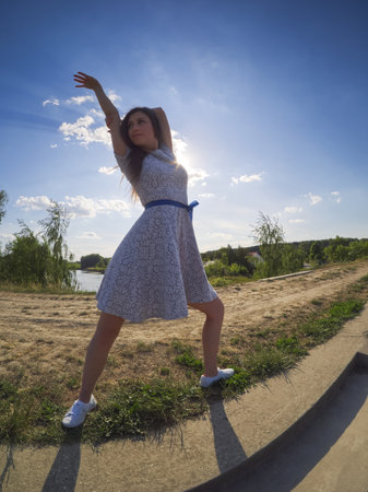A fit girl dances outdoors in a floral dress under the sunny skyの写真素材