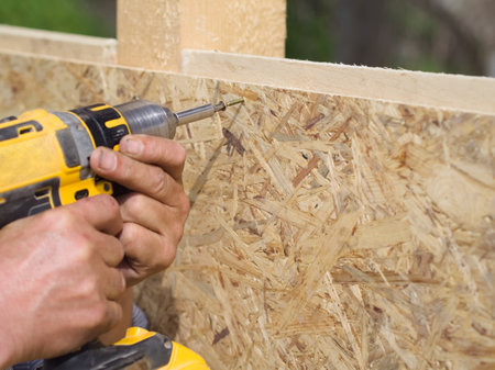 Carpenter working with yellow electric screwdriver on a wooden boardの写真素材