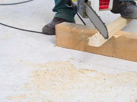 Carpenter using a chainsaw to cut a wooden board.の写真素材