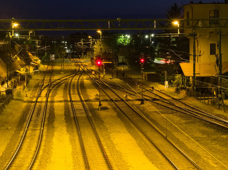 A striking nighttime view of the SiÃ³fok trainyard, with multiple tracks illuminated by yellow lights, featuring prominent red signal lights and distant buildings under a dark sky.の写真素材