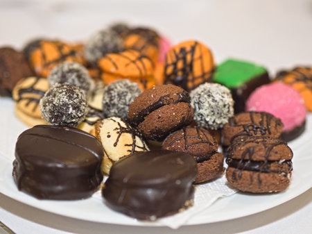 A delightful close-up of a diverse assortment of small pastries and cookies, featuring various colors, toppings, and textures, artfully arranged on a white serving plate, creating an inviting display.の写真素材