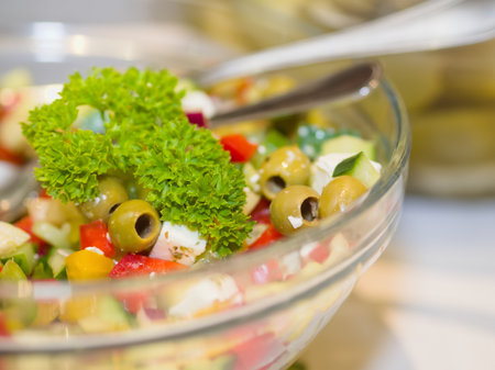 A close-up of a fresh Mediterranean salad featuring prominent green olives, colorful chopped vegetables, and a vibrant parsley garnish in a clear glass bowl, emphasizing the fresh ingredients.の写真素材