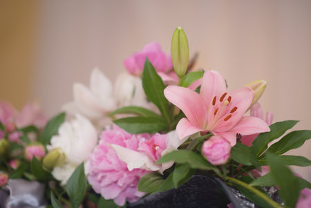 A beautiful close-up of an elegant flower bouquet featuring prominent pink lilies, soft white blooms, and lush green foliage, with hints of pink peonies, set against a gently blurred background.の写真素材