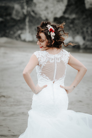 Beautiful bride on the seacoast. On the woman is a long wedding dress. Fluttering hair and flowers in her hair looking away. On the beach.の写真素材