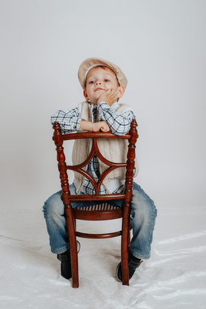 A little boy in a cap sits on a chair and thinks. On a white backgroundの写真素材