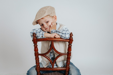 A little boy in a cap sits on a chair and thinks. On a white backgroundの写真素材