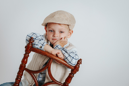 A little boy in a cap sits on a chair and thinks. On a white backgroundの写真素材