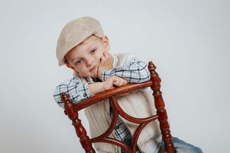 A little boy in a cap sits on a chair and thinks. On a white backgroundの写真素材