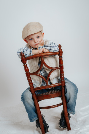 A little boy in a cap sits on a chair and thinks. On a white backgroundの写真素材
